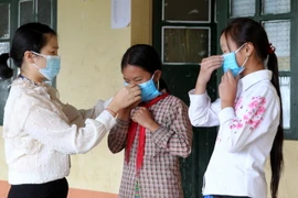 Giáo viên trường Tiểu học và Trung học cơ sở A Lù huyện Bát Xát hướng dẫn học sinh cách đeo khẩu trang đúng cách. (Ảnh: Quốc Khánh/TTXVN)