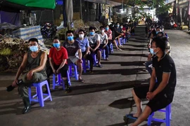 Các tiểu thương ngồi xếp hàng đảm bảo giãn khoảng cách chờ lấy mẫu xét nghiệm trong đêm. (Ảnh: Thành Đạt/TTXVN)