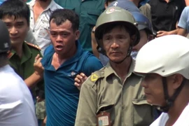 Nghi can (áo xanh) bị khống chế đưa về trụ sở. (Ảnh: Thành Chung/TTXVN)