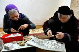 Cụ bà Nguyễn Thị Quý (phải) cùng con cháu tham gia làm quỳ phục vụ cho nghề dát vàng bạc. (Ảnh: Thanh Hà/TTXVN)