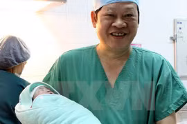 Giáo sư, tiến sỹ Nguyễn Viết Tiến, Thứ trưởng Bộ Y tế - người trực tiếp thực hiện phẫu thuật lấy thai cho ca mang thai hộ đầu tiên tại Bệnh viện Phụ sản Trung ương - bế bé gái mới sinh. (Ảnh: Dương Ngọc/TTXVN)