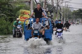 Xe ba gác làm dịch vụ vận chuyển xe máy qua đoạn ngập nước tại huyện Nhà Bè. (Ảnh: Xuân Dự/TTXVN)