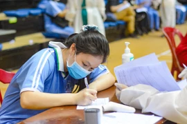 Học sinh viết vào phiếu cam kết tiêm chủng. (Ảnh: Văn Dũng/TTXVN)