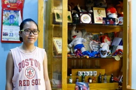 Tuệ Minh bên “bảng vàng” thành tích của cha. (Ảnh: Minh Chiến/Vietnam+)