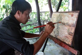 Anh Lê Hoàng Nhân phác họa bức tranh làm từ vỏ tràm. (Ảnh: Lê Sen/TTXVN)