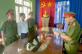 Công an đọc lệnh khởi tố bị can, bắt tạm giam đối với Phạm Đình Nhất (áo trắng). (Ảnh: TTXVN phát)
