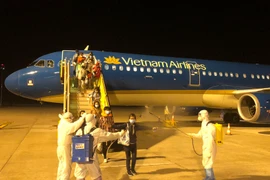 Phun khử khuẩn toàn bộ hành khách sau khi bước xuống máy bay và sau đó được đưa đi cách ly tập trung nhằm phòng chống COVID-19. (Ảnh: CTV/Vietnam+)