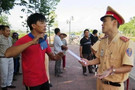 Lái xe Chính (áo đỏ) lấy điện thoại di động ra để quay lại lực lượng chức năng đang làm nhiệm vụ. (Ảnh: Phan Quân/Vietnam+)