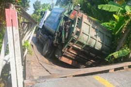 Hiện trường xe rác làm sập cầu và bị mắc kẹt giữa cầu. (Ảnh: TTXVN phát)