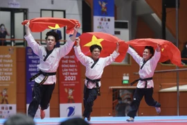 Ba vận động viên Việt Nam là Trần Hồ Duy, Nguyễn Đình Khôi, Nguyễn Thiên Phụng giương cao 3 lá cờ Tổ quốc chạy quanh nhà thi đấu sau khi xuất sắc giành huy chương Vàng nội dung biểu diễn Quyền đồng đội nam. (Ảnh: Minh Quyết/TTXVN) 