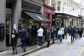 Người dân xếp hàng mua đồ bên ngoài một cửa hàng ở London (Anh). (Ảnh: AFP/TTXVN)