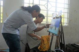 Thầy Nguyễn Văn Hoàng tỉ mỉ hướng dẫn học sinh của mình cách chọn phối màu. (Ảnh: Thu Hoài/TTXVN)