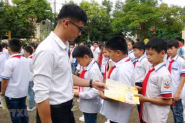 Cán bộ bảo hiểm phát tờ rơi tuyên truyền về bảo hiểm y tế học sinh. (Ảnh: Hữu Quyết/TTXVN) 