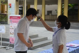 Thí sinh được đo thân nhiệt, rửa tay bằng nước sát khuẩn, thay khẩu trang mới tại cổng điểm thi. (Ảnh: Văn Dũng/TTXVN)