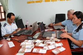 Cán bộ Hải quan cửa khẩu Mộc Bài kiểm tra số lượng tiền bath Thái Lan thu giữ. (Ảnh: Lê Đức Hoảnh/TTXVN)
