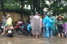 Do sân trước điểm thi của Trung tâm giáo dục thường xuyên Thanh Trì không có mái che, nên tất cả các phụ huynh đều phải mặc áo mưa. (Ảnh: Sơn Bách/Vietnam+)