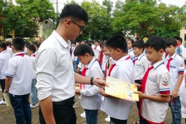 Cán bộ bảo hiểm phát tờ rơi tuyên truyền về bảo hiểm y tế học sinh. (Ảnh: Hữu Quyết/TTXVN)