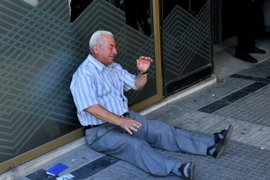 Một người dân Hy Lạp ngồi bên ngoài chi nhánh ngân hàng ở Thessaloniki chờ rút tiền. (Nguồn: AFP/TTXVN) 