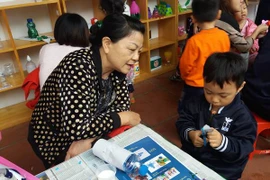 Một học sinh mầm non chăm chú cắt giấy để trang trí cho lọ hoa sẽ được làm từ vỏ chai nước ngọt. (Ảnh: PM/Vietnam+)