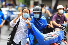 Phụ huynh trùm áo mưa chở con đi thi tuyển sinh lớp 10 sáng 12/6. (Ảnh: TTXVN)