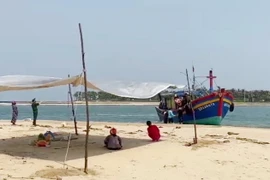 Người nhà nạn nhân và các lực lượng chức năng đưa thi thể ngư dân vào bờ. (Ảnh: TTXVN phát)