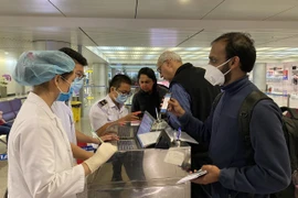 Nhân viên Trung tâm Kiểm dịch y tế quốc tế hướng dẫn hành khách thực hiện tờ khai y tế trước khi làm thủ tục nhập cảnh tại sân bay Tân Sơn Nhất Thành phố Hồ Chí Minh. (Nguồn: TTXVN phát)