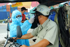 Nhân viên y tế đo thân nhiệt người ra vào Thành phố Hồ Chí Minh tại chốt kiểm dịch. (Ảnh: Đinh Hằng/TTXVN)
