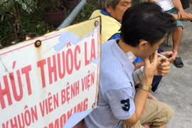 Vô tư nhả khói trong khuôn viên bệnh viện dù bảng cấm hút thuốc ngay bên cạnh. (Ảnh: Đinh Hằng/TTXVN)