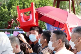 Một người xếp hàng mua vé dùng ghế để che nắng, chờ đến lượt được mua vé. 