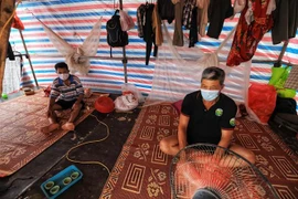 Dưới nắng Hè gay gắt, những người thợ xây dựng, phụ hồ quanh quẩn bên trong lán trại hơn 10m2, dựng tạm bợ bằng mấy tấm gỗ và phủ bạt. (Ảnh: Thành Đạt/TTXVN) 