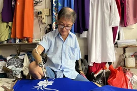 Ông Trần Hùng Bảo vẽ hoa trên áo cho khách. (Ảnh: Ánh Tuyết/TTXVN) 