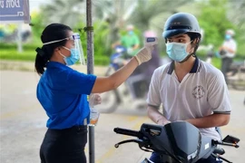 Tình nguyện viên đo thân nhiệt cho thí sinh. (Ảnh: Hữu Chí/TTXVN) 