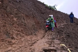 Các giáo viên điểm trường mầm non Hoa Đào, xã Suối Bâu, huyện Phù Yên dắt xe máy qua điểm sạt lở. (Ảnh: Hữu Quyết/TTXVN)