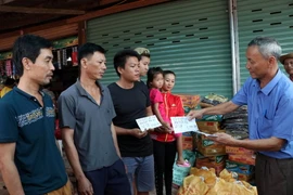 Chủ tịch Hội người Việt Nam tại tỉnh Attapeu Võ Văn Mừng trao tặng số tiền 1 triệu Kip cho 3 gia đình bị ảnh hưởng sau sự cố vỡ đập thủy điện. (Ảnh: Quang Thái/TTXVN)
