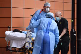 Nhân viên y tế chuyển bệnh nhân COVID-19 tới bệnh viện ở London, Anh. (Ảnh: AFP/TTXVN)
