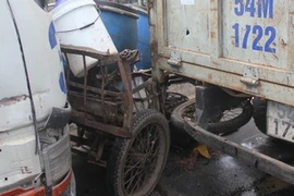 Chiếc xe ba gác bị kẹp cứng ở giữa hai chiếc xe tải. (Ảnh: Hoàng Tuấn/Vietnam+) 
