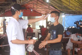Người dân được kiểm tra thân nhiệt tại chốt kiểm soát dịch bệnh. (Ảnh: Tuấn Anh/TTXVN)
