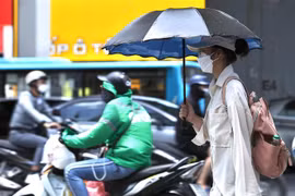Người dân sử dụng ô, quần áo chống nóng khi phải di chuyển ngoài trời. (Ảnh: Hoàng Hiếu/TTXVN)