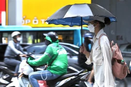 Người dân sử dụng ô, quần áo chống nóng khi phải di chuyển ngoài trời. (Ảnh: Hoàng Hiếu/TTXVN)