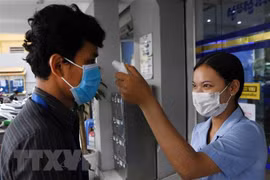 Kiểm tra thân nhiệt người dân trước cửa một ngân hàng nhằm phòng dịch COVID-19 lây lan, tại Phnom Penh, Campuchia. (Ảnh: AFP/TTXVN)