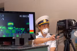 Kiểm tra thân nhiệt hành khách ở cửa khẩu Nội Bài. (Ảnh: TTXVN)