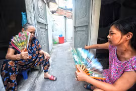 Nhiều bệnh nhân ở xóm chạy thận Lê Thanh Nghị chọn cách ra cửa ngồi quạt tay để chống chọi với cái nóng như thiêu đốt trong những căn phòng trọ chật hẹp. (Ảnh: Thành Đạt/TTXVN)