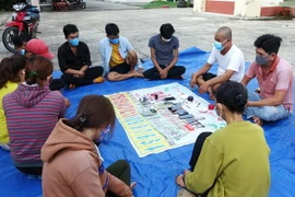 Các đối tượng tham gia đánh bạc bị bắt giữ cùng tang vật. (Ảnh: Thanh Tân/TTXVN)
