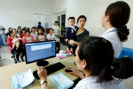 Nhân viên y tế làm thủ tục tiêm chủng cho trẻ tại Trung tâm Y tế Dự phòng Hà Nội. (Ảnh: Dương Ngọc/TTXVN)