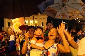 Người dân đứng tại Quảng trường Cánh mạng Tháng Tám xem bắn pháo hoa khu vực Hồ Hoàn Kiếm (Hà Nội). (Ảnh: Quý Trung/TTXVN)