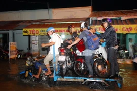 Nhiều xe ba gác máy vận chuyển xe máy của người dân qua điểm ngập sâu. (Ảnh: Mạnh Linh/TTXVN)