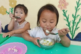 Bữa ăn bán trú của học sinh điểm trường Sáng Xoáy. Không có điện, để thoáng mát, các em ăn bữa trưa ở ngay hàng lang lớp học. (Ảnh: Phạm Mai/Vietnam+)