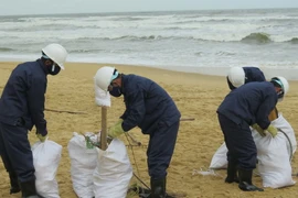Thu gom dầu vón cục, rác thải dạt vào bờ biển huyện Núi Thành. (Ảnh: Đoàn Hữu Trung/TTXVN)