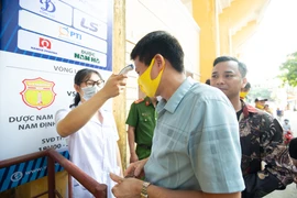 Cổ động viên phải đeo khẩu trang, rửa tay bằng dung dịch sát khuẩn và được đo thân nhiệt trước khi vào sân Thiên Trường theo dõi bóng đá. (Ảnh: Nguyên An/Vietnam+)