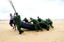 Cán bộ, chiến sỹ Đồn Biên phòng Lý Hòa (Bộ đội Biên phòng Quảng Bình) giúp ngư dân xã Đức Trạch, huyện Bố Trạch, tỉnh Quảng Bình đưa thuyền lên bờ tránh trú. (Ảnh: TTXVN phát)